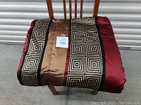 Comforter folded and placed on a chair, shows front with geometric square pattern in black and cream on brown and burgundy sections.