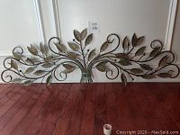Full view of metal wall art with leaf design in front of white wall, showing size and detail.