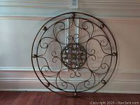 Front view of the round metal decorative wall artwork showing the intricate floral center and surrounding scroll patterns with metal orb accents around the edge.