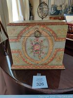 Front view of decorative painted wooden box featuring central floral medallion with ring pull handle.