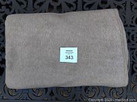 Folded beige polyester fleece blanket on black metal background, clear view of blanket texture and color, showing general condition.