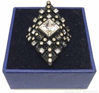 Front view of the ring in a blue box showing the large square clear crystal centerpiece with smaller clear and coloured crystals on black rhodium plating.