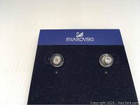 Front view of the Swarovski pierced earrings with clear crystals set in bezel style, mounted on branded card.