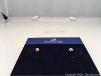 Front view showing pair of small Swarovski crystal stud earrings mounted on navy blue branded display card.