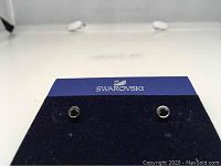 Pair of Swarovski black Harley medium stud earrings displayed on a blue Swarovski branded card, showing the front view with shiny black crystals.