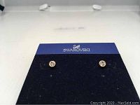 Pair of Swarovski Harley gold plated pierced stud earrings with medium-sized clear crystals on blue display card with Swarovski logo.