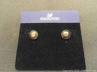 Front view of a pair of light pink Swarovski crystal stud earrings displayed on branded card.