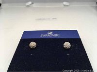 Pair of round Swarovski stud earrings with white crystals set in 9CT gold shown on black and blue Swarovski branded display card.