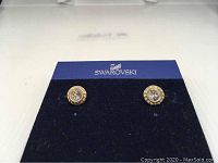 Pair of Swarovski gold plated stud earrings on dark blue card with Swarovski logo, clear crystals and smaller crystal pavé shown. Some pavé crystals missing.