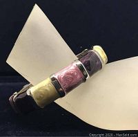 Side angle view of the brass colored bracelet showing patterned colored enamel panels in pink, yellow, and purple.