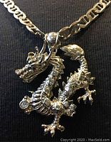 Close-up photo of silver-tone dragon pendant with clear crystals on silver chain