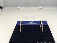 Pair of Swarovski Devin Rose sterling silver large hoop earrings with Swarovski crystals displayed on a velvet SWAROVSKI card. Earrings are silver colored with clear round crystals.
