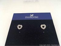Swarovski heart-shaped crystal earrings displayed on a black and blue card with Swarovski branding.