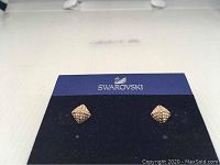 Pair of rose gold tone Swarovski earrings in pavé diamond shape on a blue Swarovski branded card.