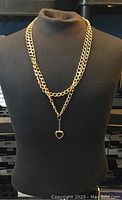 Gold colored chain displayed on a black bust form showing it worn as a long single chain with gold heart pendant visible.