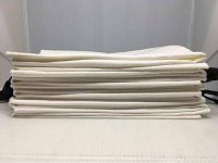 Stack of 10 folded white microfibre golf towels viewed from the side showing towel thickness and textile texture.