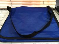 Blue nylon tote bags stacked, showing the fabric texture and black shoulder straps.