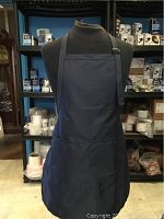 Front view of single blue nylon apron displayed on mannequin showing full apron with neck strap and pocket.