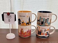 Front stacked view of four Starbucks You Are Here mugs showing city designs for New York, Nashville, Twin Cities and Detroit