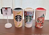 Front view of three Starbucks collectible travel mugs showing banana and floral designs