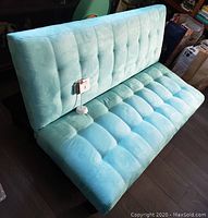 Front-side angle of light blue children's futon chair with tufted cushion and black legs.