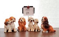 Front view of the four ceramic dog figurines arranged side by side with MaxSold auction card behind them.