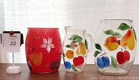 Two large Bartlett Collins cookie jars without lids and one juice pitcher, all hand-painted with colorful fruit designs.