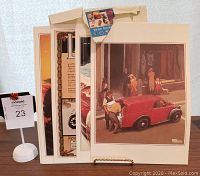 Eight vintage automotive poster reprints fanned out standing next to MaxSold label 23, showing art style and size.