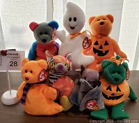 All 7 TY Halloween Beanie Baby bears arranged in two rows on a table showing front view including a white ghost, orange pumpkin bears and colorful patchwork bear.