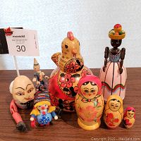 Front view of seven wooden vintage European collectible figures including a large colorful nested doll, a chicken, a tall woman figure with basket, clown, and others arranged on a table.