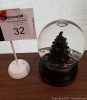 Photo of Christmas snow globe with internal Christmas tree and glitter, showing black base.