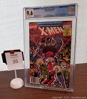 Front view of X-Men Annual #14 comic book in a CGC graded 9.6 protective slab with MaxSold lot number sign beside it.