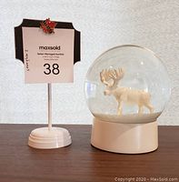 Front view of the snow globe with white moose inside clear glass dome on white base, shown next to auction lot number display.