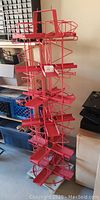 Full view of 66 inch tall red metal spinner rack with multiple shelves for books or other display items, showing structure and weighted base.