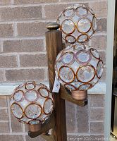 Close-up of two spherical glass globe shades with amber circular accents mounted on the wooden arms of the lamp.