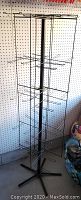 Full view of black metal spinner rack showing the vertical pole and horizontal arms setup for hanging various display items.