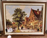 Full view of framed cross stitch artwork showing Amsterdam street scene with gabled buildings, tree and people.