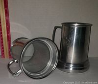 Two vintage pewter steins with clear bottoms, one standing, one lying flat to show base and handle