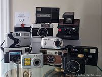 Lot of nine vintage cameras in a group showing different brands and styles, placed on boxes and table