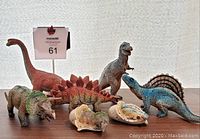 Seven AAA branded toy dinosaurs including two baby dinosaurs in eggs, displayed on a white background for detail.