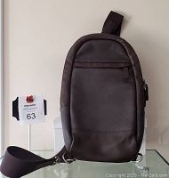 Front view of brown leather saddle bag showing front zip pocket and attached adjustable fabric strap with metal rings.