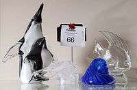 Group photo of all five art glass pieces: two penguins with baby, clear fish, polar bear, and blue seashell on white background.