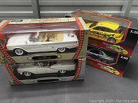 Four die cast model cars in original or display boxes. Two classic car models and two racing cars in packaging.