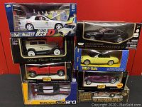 Lot of seven die cast model cars in original packaging stacked on red background showing various models and brands including a white Initial D Mazda RX-7 and red F-350 pickup by Maisto.