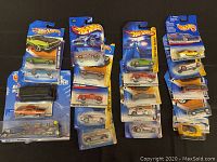 Lot of 15 packaged Hot Wheels metal toy cars shown spread out on dark surface to display overall quantity and packaging condition.