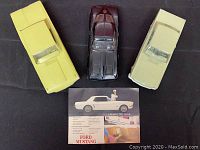 Top-down photo of three diecast model cars: yellow and cream Ford Mustangs and a dark red Chevrolet Corvette with original Ford Mustang brochure in front.