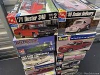 Stack of 7 plastic car model kits from AMT and Revell showing the front of boxes with artwork and skill level 2.