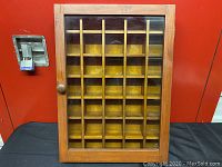 Front view of wooden case showing 30 compartments behind glass door.