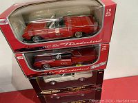 Three boxed cars stacked: two red 1963 Ford Thunderbirds and one 1967 Shelby model in black American Muscle packaging