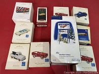 Overview of all collectible car-themed Christmas tree ornaments in original boxes plus one billboard ornament from Snow Village collection.
